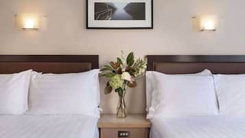 Una camera d'albergo con due letti, un comodino con un vaso di fiori e un quadro appeso al muro.