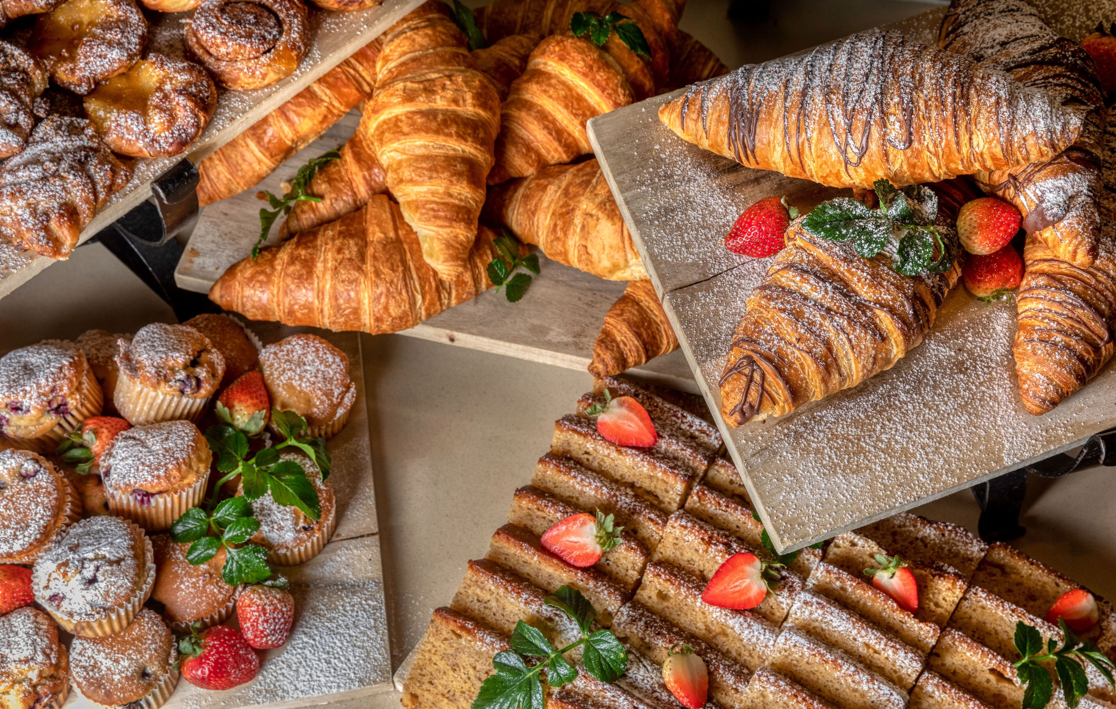 Variedad de pastelería, incluyendo croissants y muffins, algunos cubiertos con fresas y azúcar glas.