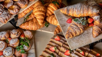 A variety of pastries including croissants and muffins, some topped with strawberries and powdered sugar.