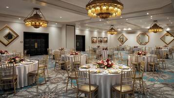 Un salón de banquetes con mesas redondas, sillas doradas y candelabros elaborados.
