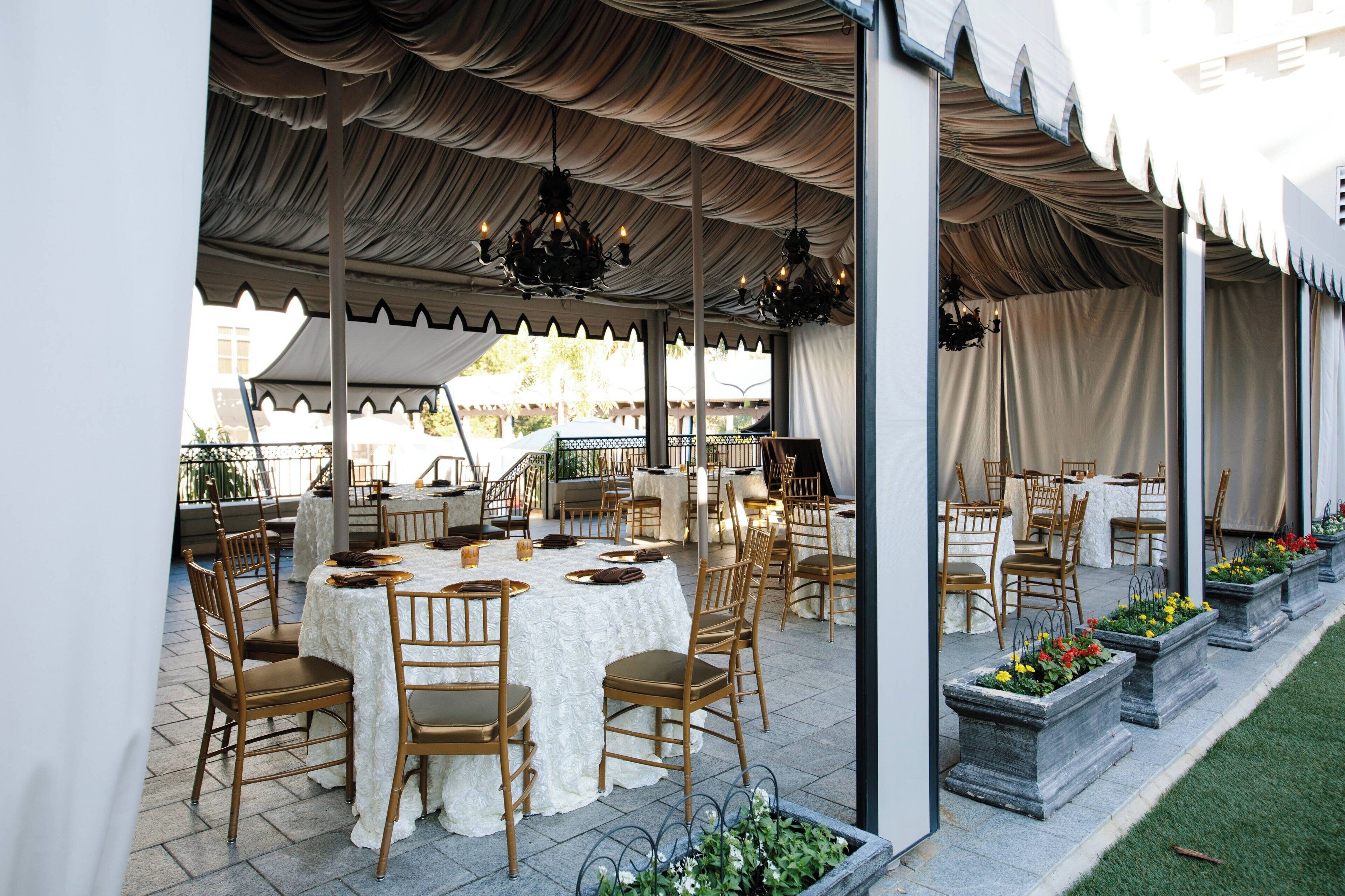 An outdoor dining area with round tables and chairs, covered by a large tent.