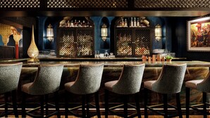 A bar with a dark blue wall, ornate wooden panels, and a marble counter. There are six bar stools with patterned upholstery. - Casa Monica Resort & Spa, Autograph Collection (St. Augustine)