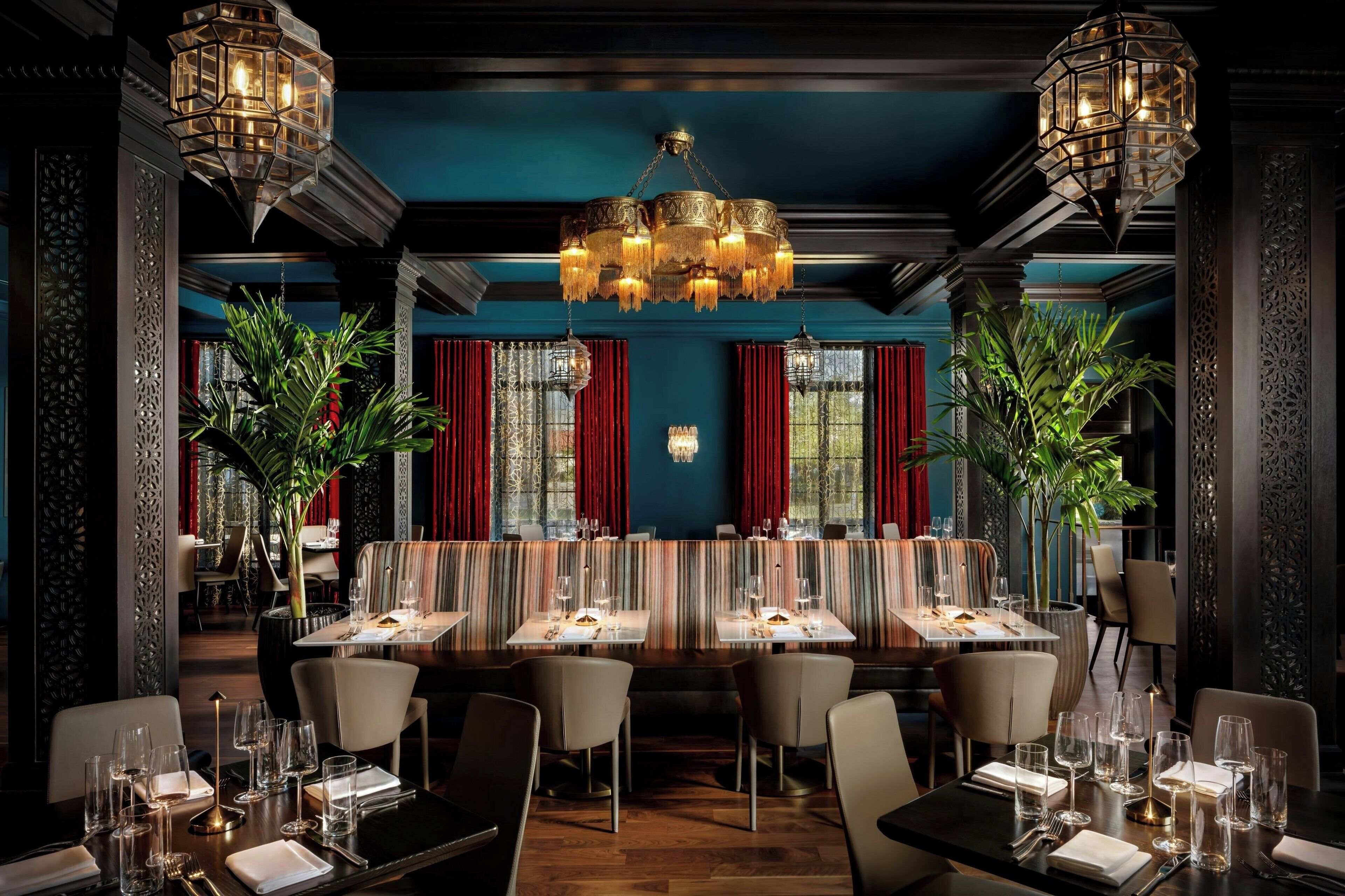 A restaurant with a long communal table, individual dining booths, and a chandelier.