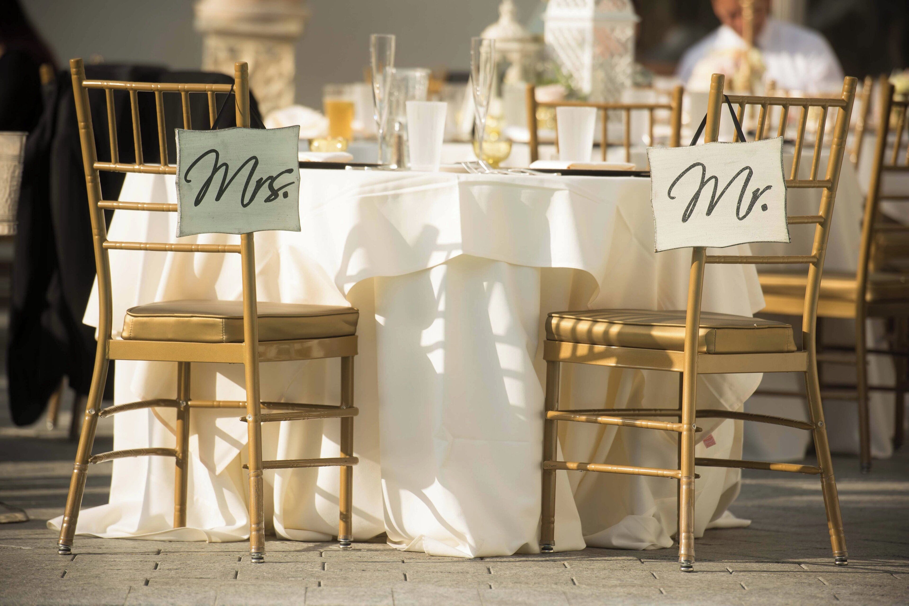A table set with white tablecloths and gold chairs, each with a name tag.