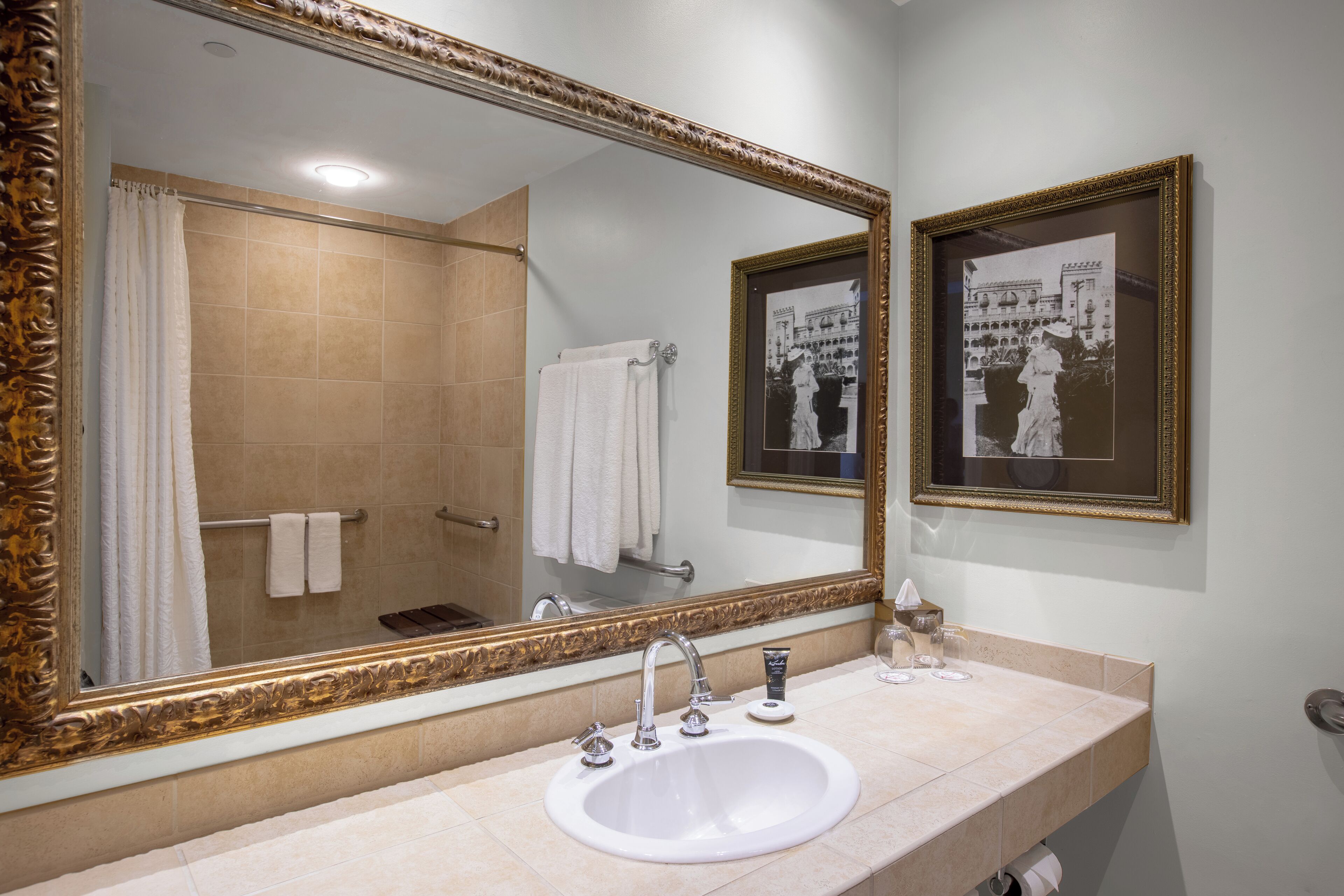 A bathroom with a large mirror, a sink, and a framed photograph on the wall.