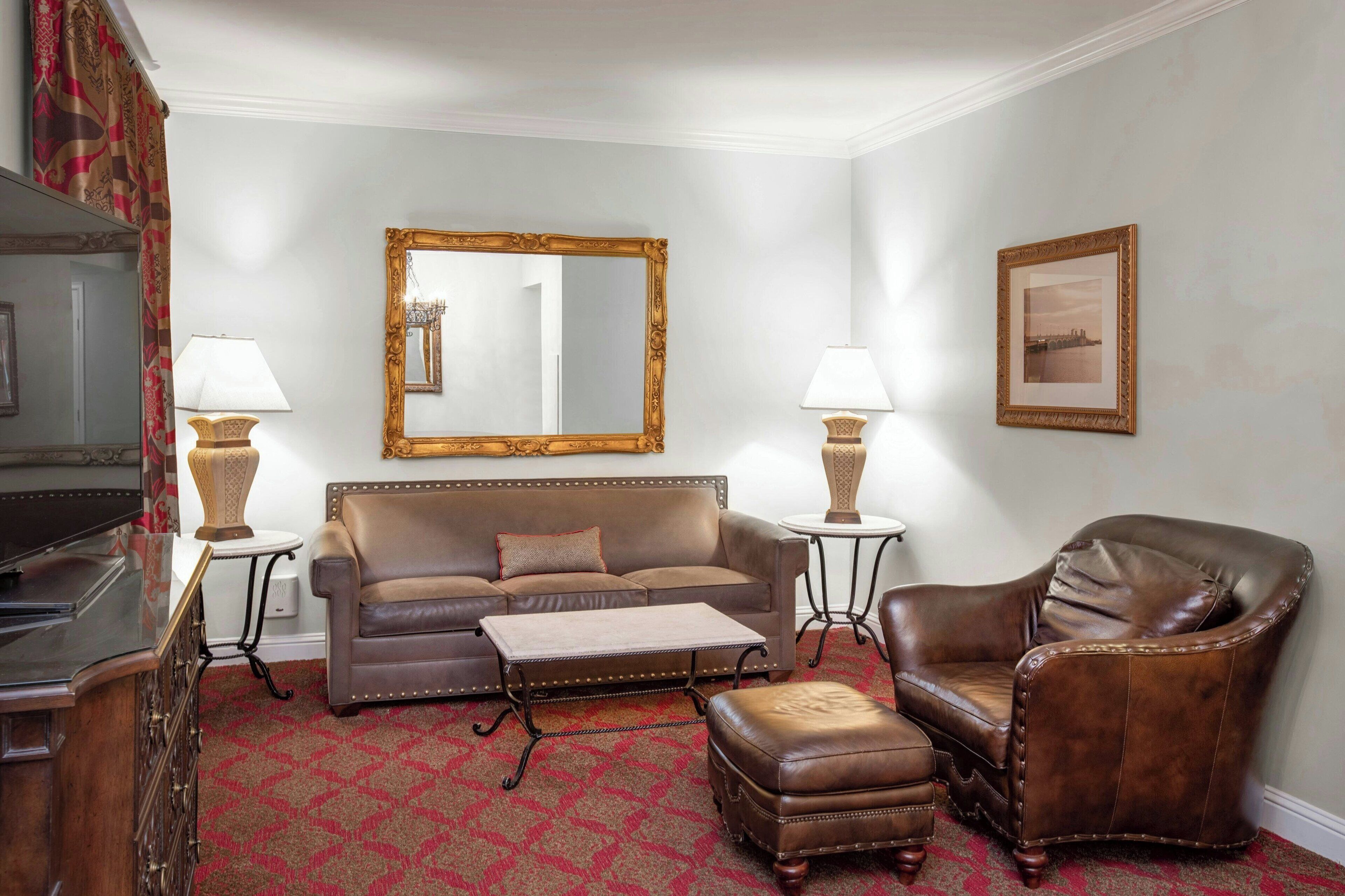 A living room with a brown leather sofa, a matching armchair, a coffee table, and two lamps. A large mirror hangs on the wall above the sofa.