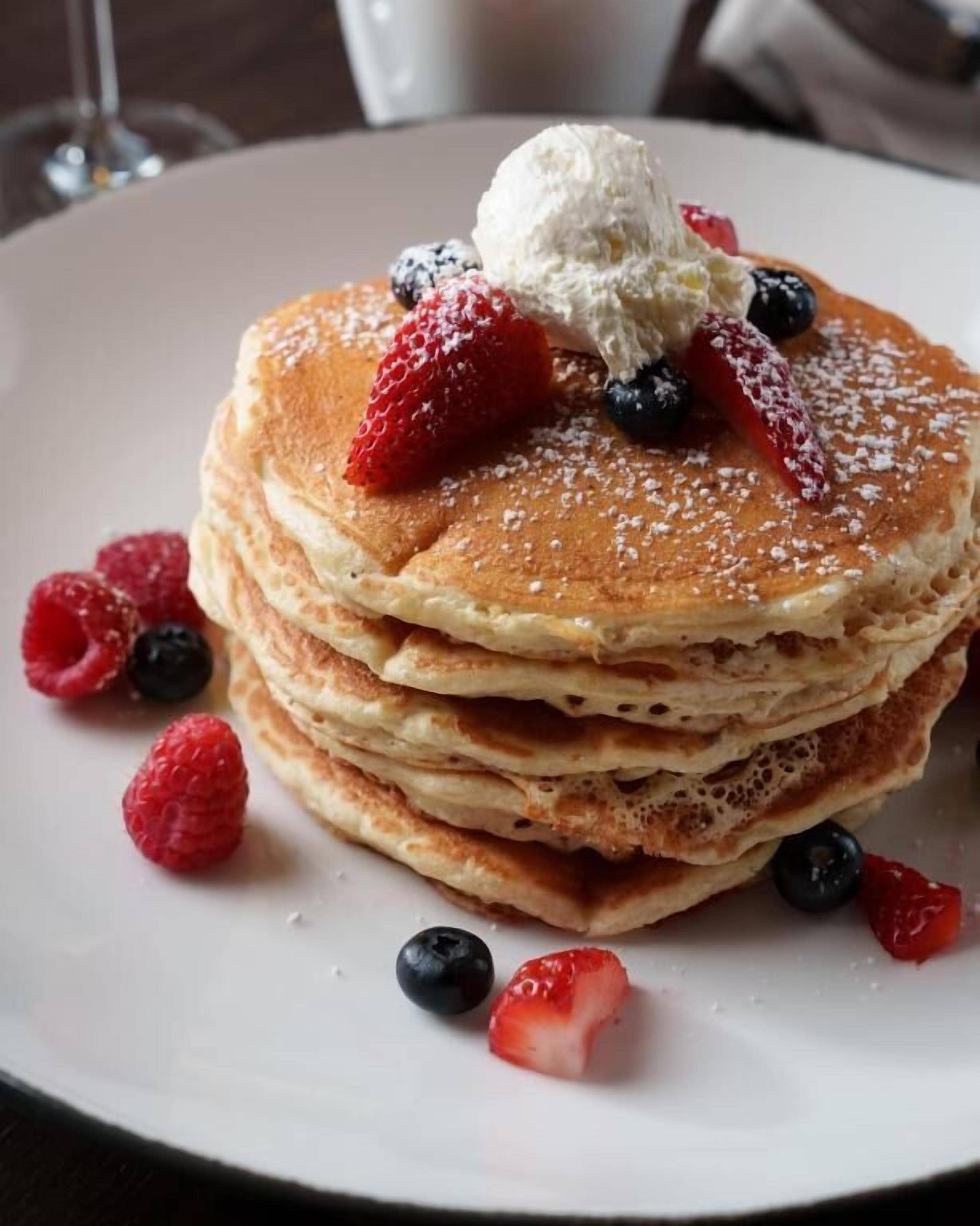A stack of pancakes with berries and whipped cream on a plate.