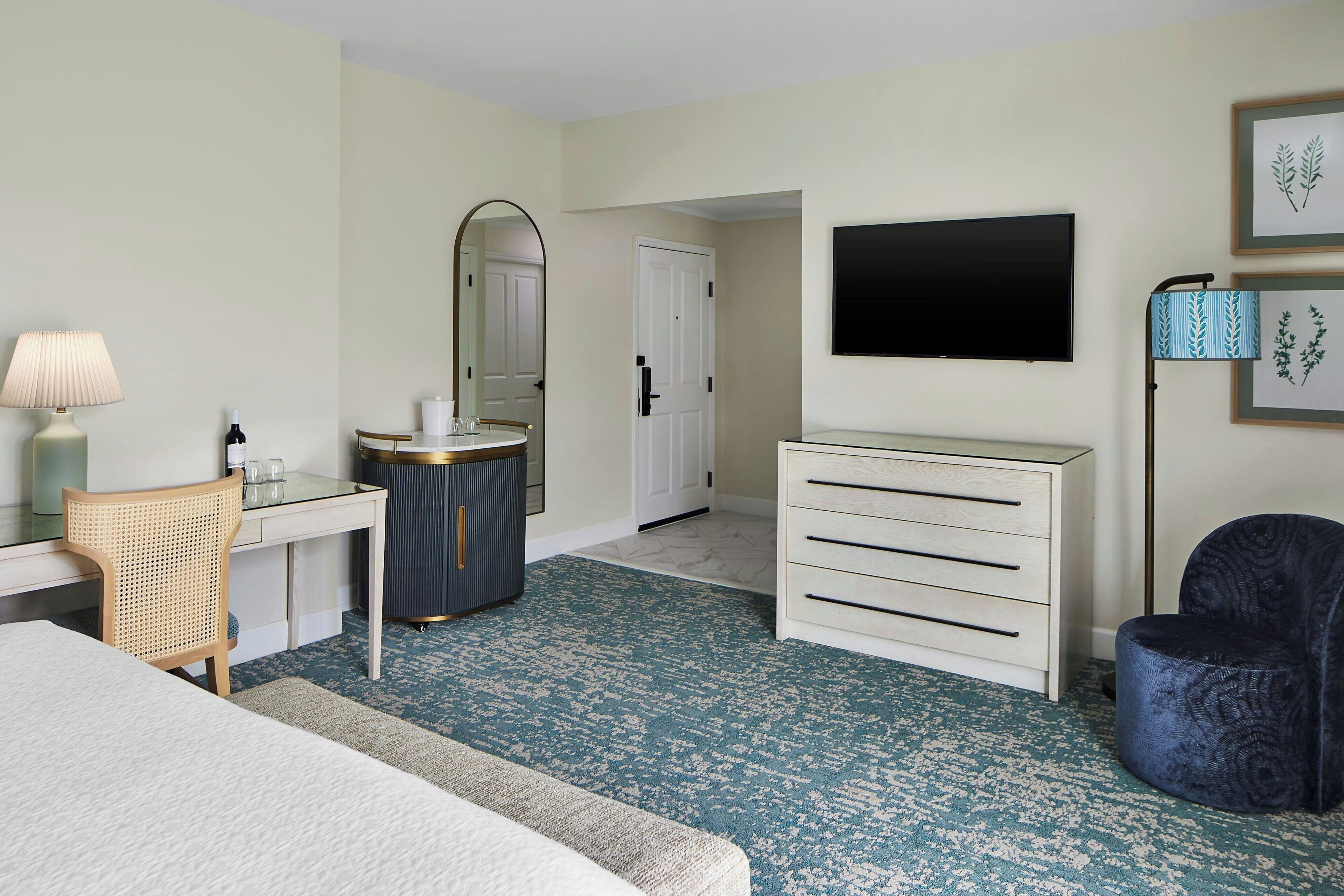 Habitación de hotel con cama, escritorio con lámpara, cómoda, televisor y una silla.