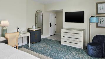 Habitación de hotel con cama, escritorio con lámpara, cómoda, televisor y una silla.