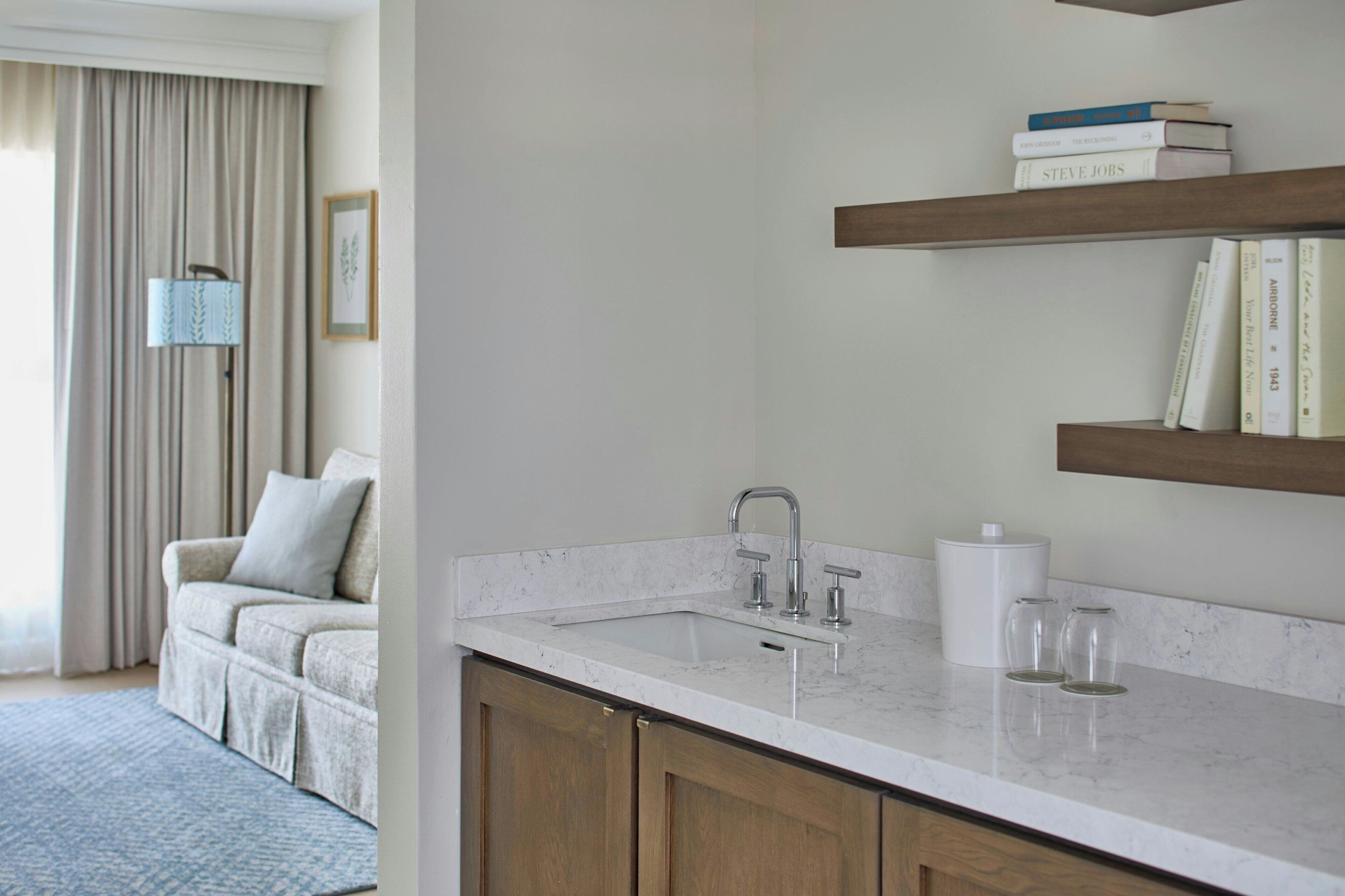 A modern kitchen with a white countertop, wooden cabinets, a built-in sink, and a bookshelf above the counter.