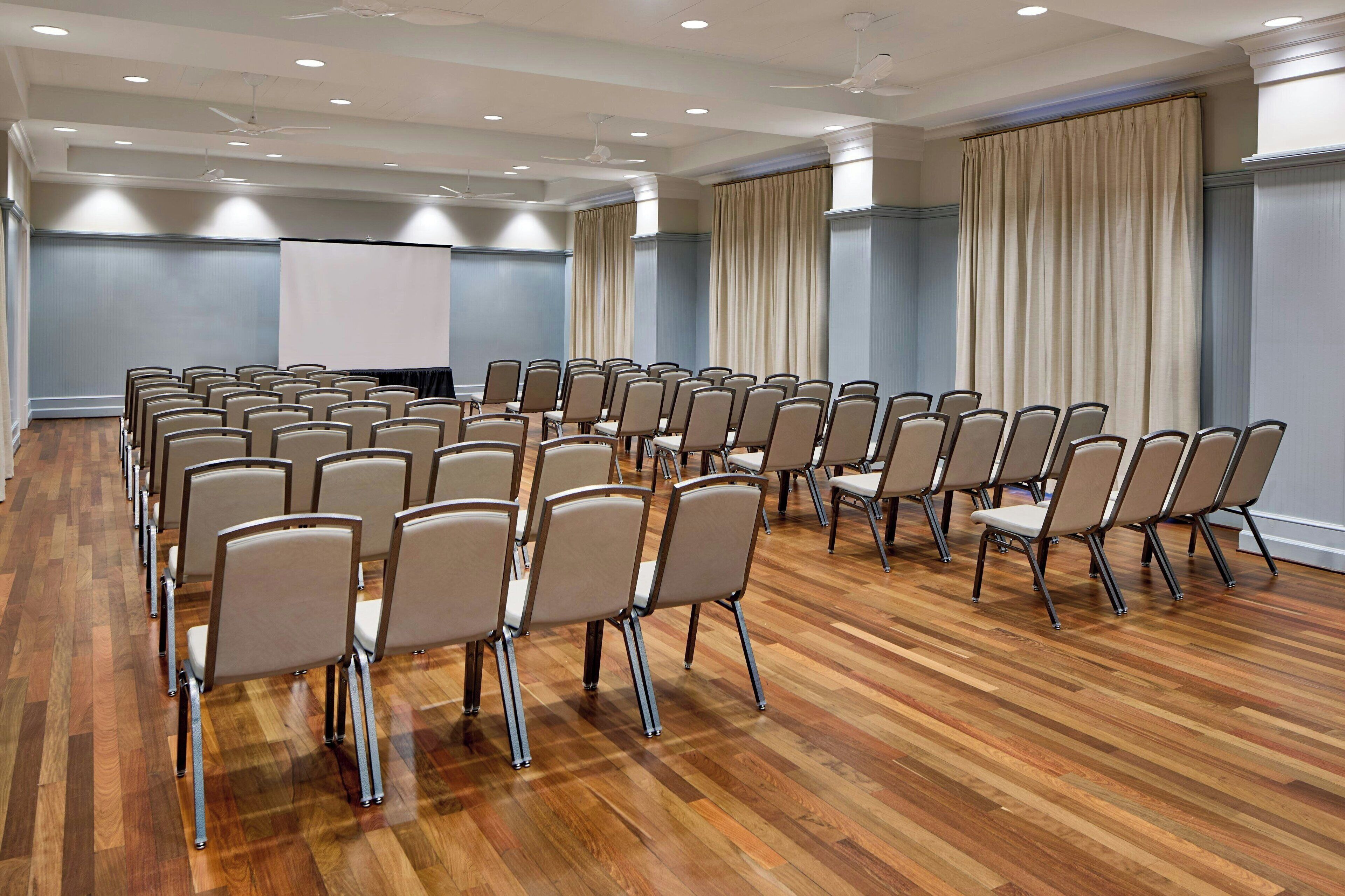 A conference room with rows of chairs, a projector screen, and a large window with curtains.