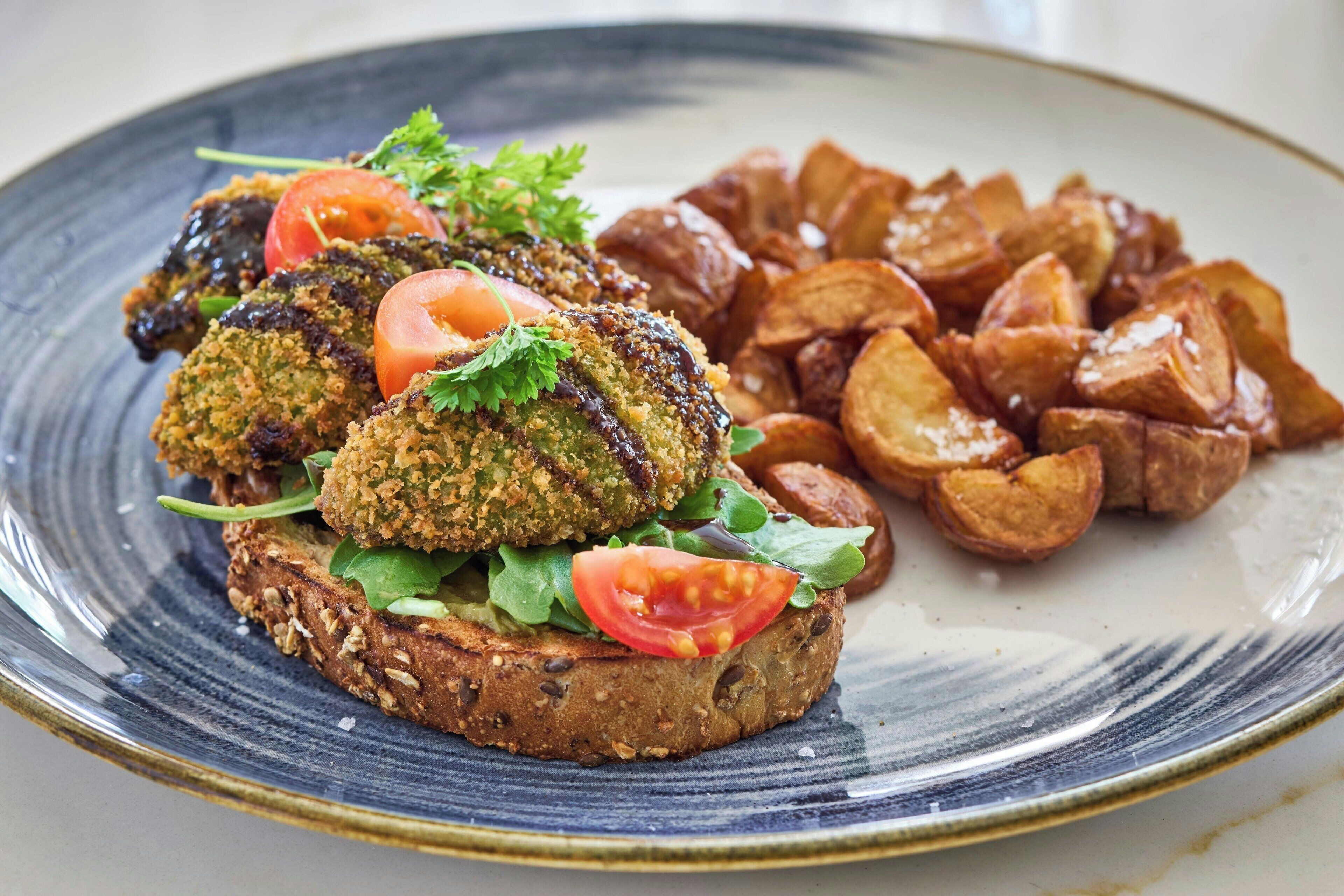 A plate with a sandwich, a slice of tomato, and roasted potatoes.