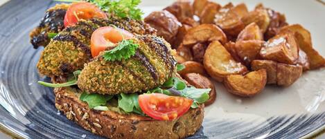 A plate with a sandwich, a slice of tomato, and roasted potatoes.