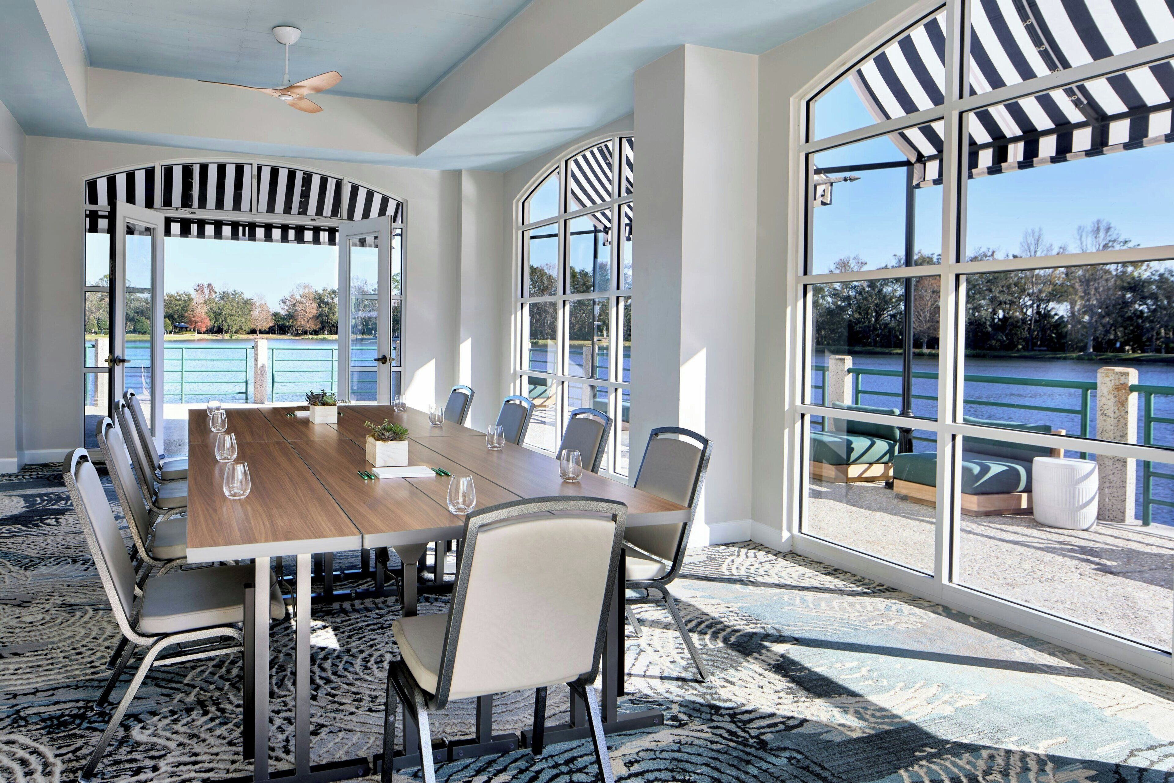 A conference room with a large table, chairs, and large windows overlooking a body of water.