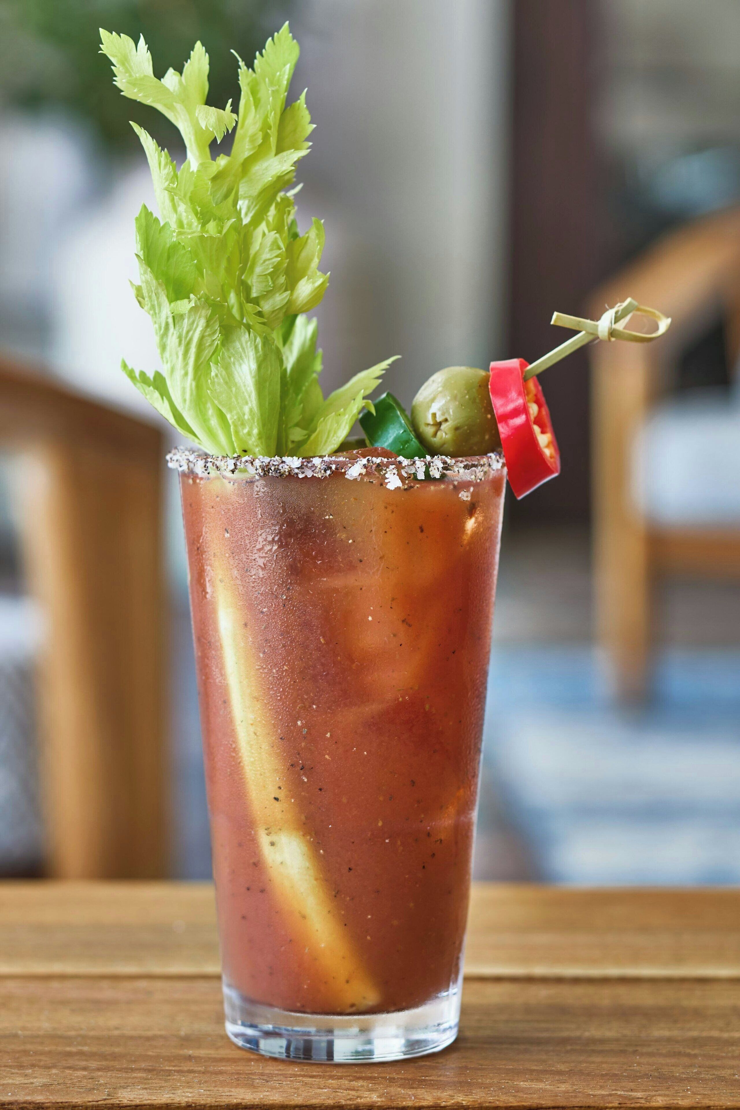 Cóctel Bloody Mary en un vaso, adornado con apio, una aceituna y un chile rojo.