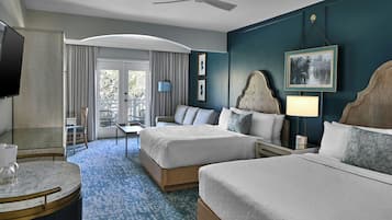 A hotel room with two beds, a TV, a ceiling fan, a balcony with a chair, and a dining area with a table and chairs.