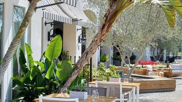An outdoor seating area with tables and chairs, surrounded by lush greenery and a palm tree.
