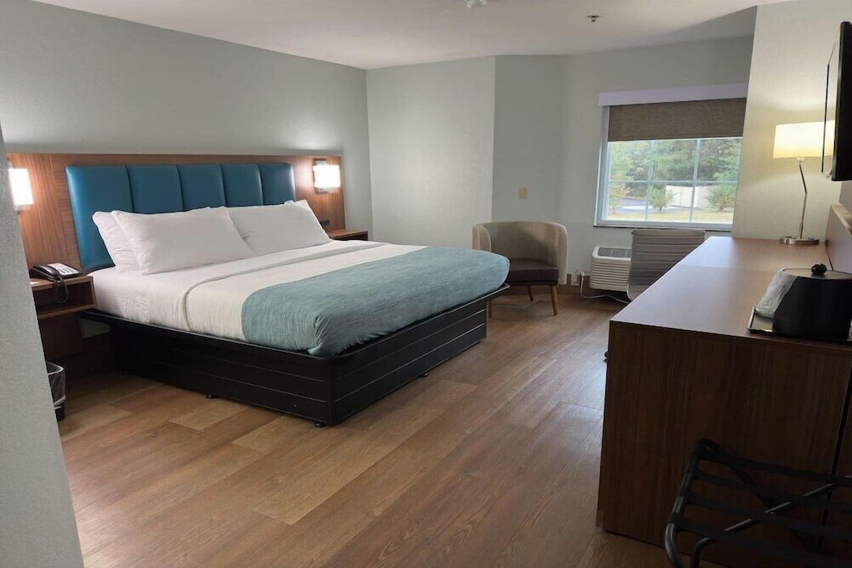 A hotel room with a bed, a desk, a chair, a TV, and a window.