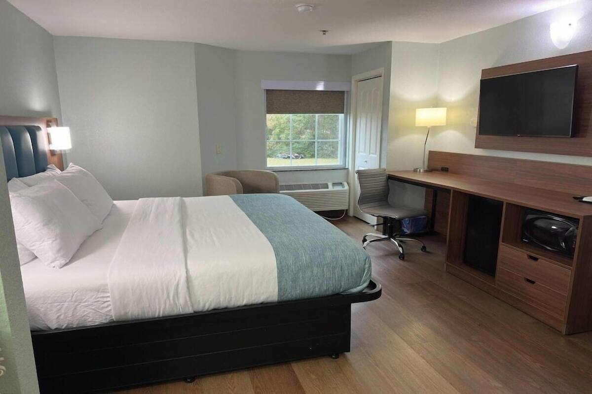 A hotel room with a bed, desk, chair, TV, and window.