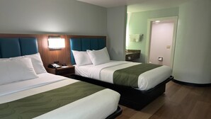 Camera d'albergo con due letti, una testiera in legno, un comodino, uno specchio nel bagno e una porta.