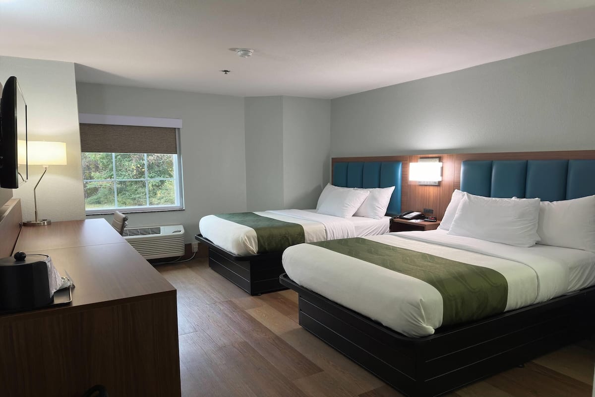 A hotel room with two beds, a desk, a lamp, and a window.