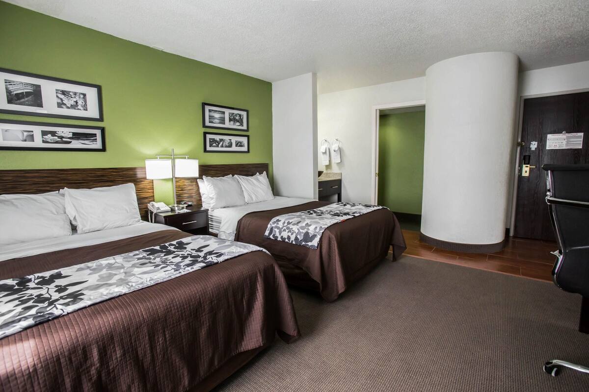 A hotel room with two beds, a nightstand, a lamp, and framed pictures on the wall.