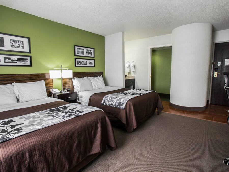 A hotel room with two beds, a nightstand, a lamp, and framed pictures on the wall.