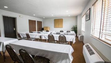 Sala de conferência com várias mesas e cadeiras, uma porta, um respiradouro e uma janela com persianas.