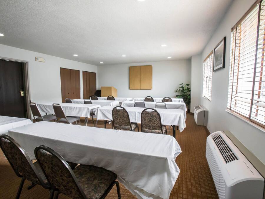 Sala de conferência com várias mesas e cadeiras, uma porta, um respiradouro e uma janela com persianas.