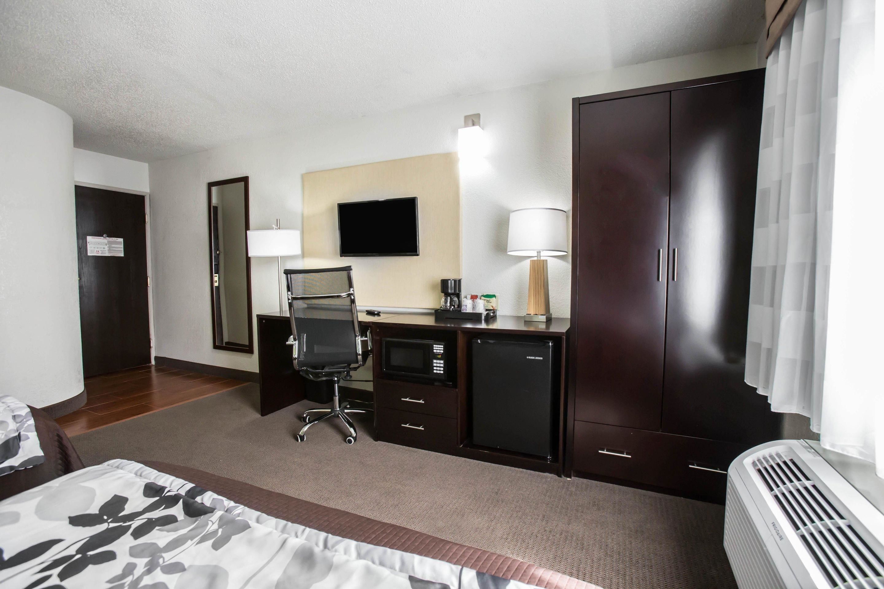 Habitación de hotel con cama, escritorio, silla, televisor, armario y aire acondicionado.
