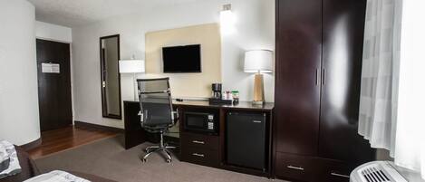 Habitación de hotel con cama, escritorio, silla, televisor, armario y aire acondicionado.