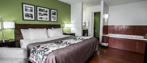 A hotel room with a large bed, a sitting area, a bathroom with a bathtub, and framed pictures on the wall.