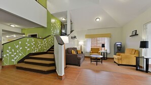 Un salon spacieux avec un escalier, un canapé, un fauteuil jaune et une petite table.