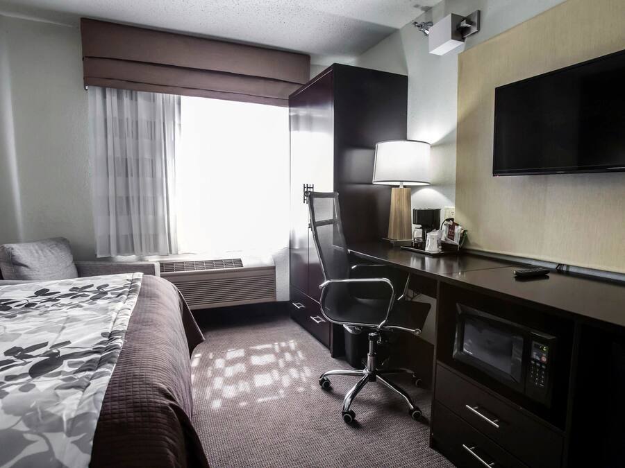 Ein Hotelzimmer mit Bett, Schreibtisch mit Stuhl, Fernseher, Lampe und einer Mikrowelle.