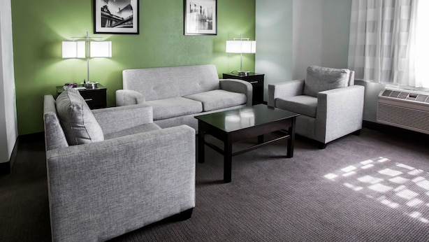Un salon moderne avec un canapé gris, une table basse et deux petites tables d’appoint avec des lampes. Deux tableaux encadrés sont accrochés au mur vert.