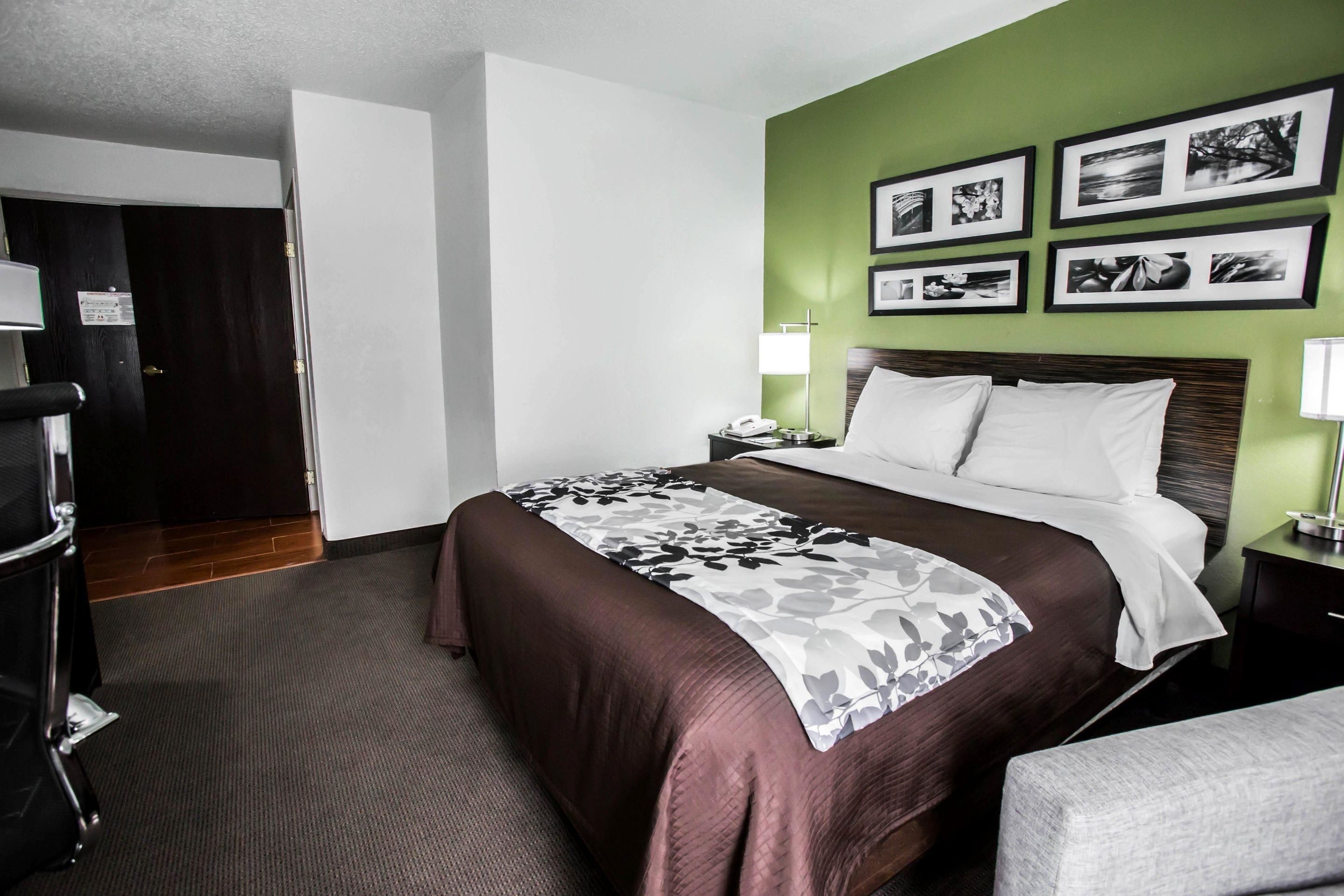 A hotel room with a bed, bedside tables, a desk, and a chair. There are framed pictures on the wall.