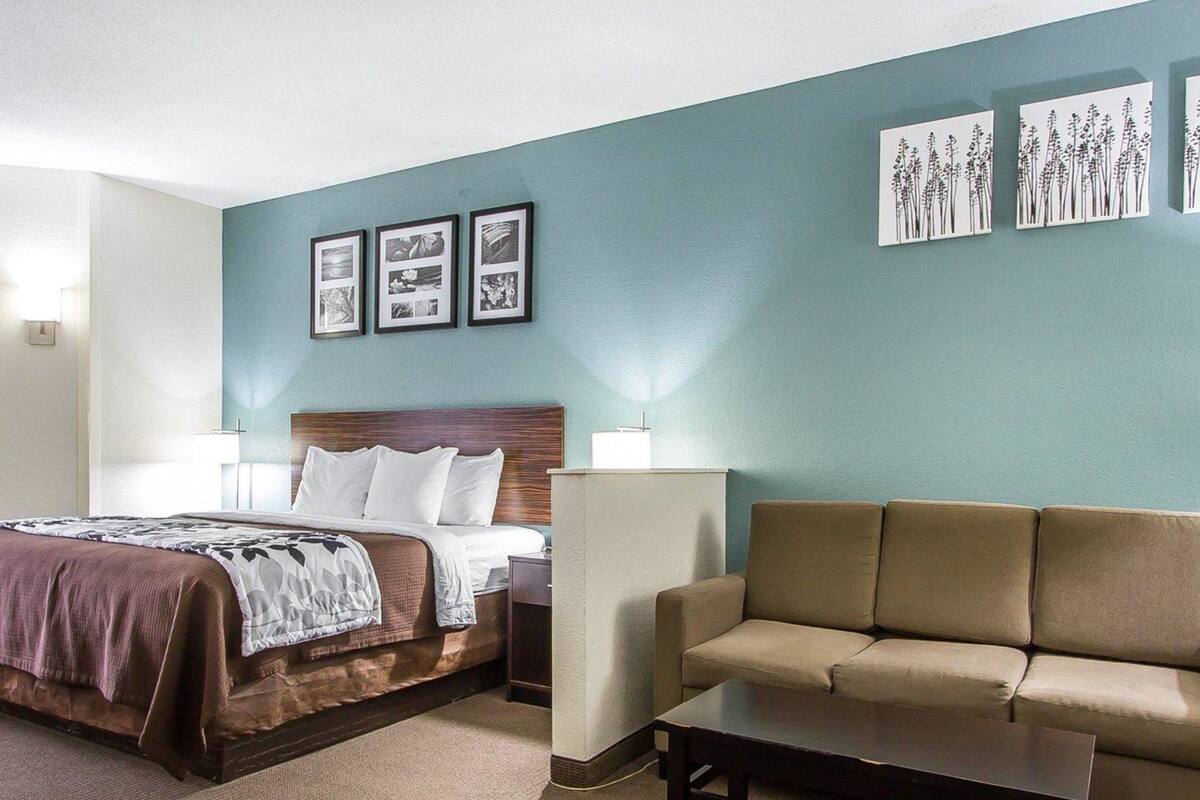 Quarto de hotel com cama, sofá, mesa de centro e obras de arte nas paredes.
