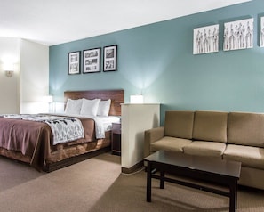 A hotel room with a bed, a sofa, a coffee table, and wall art. - Sleep Inn Scott/Lafayette West (Scott)