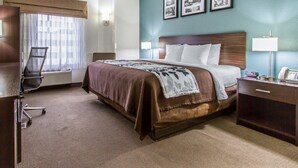 Een hotelkamer met een groot bed, een bureau met lamp, een stoel en een raam met gordijnen.