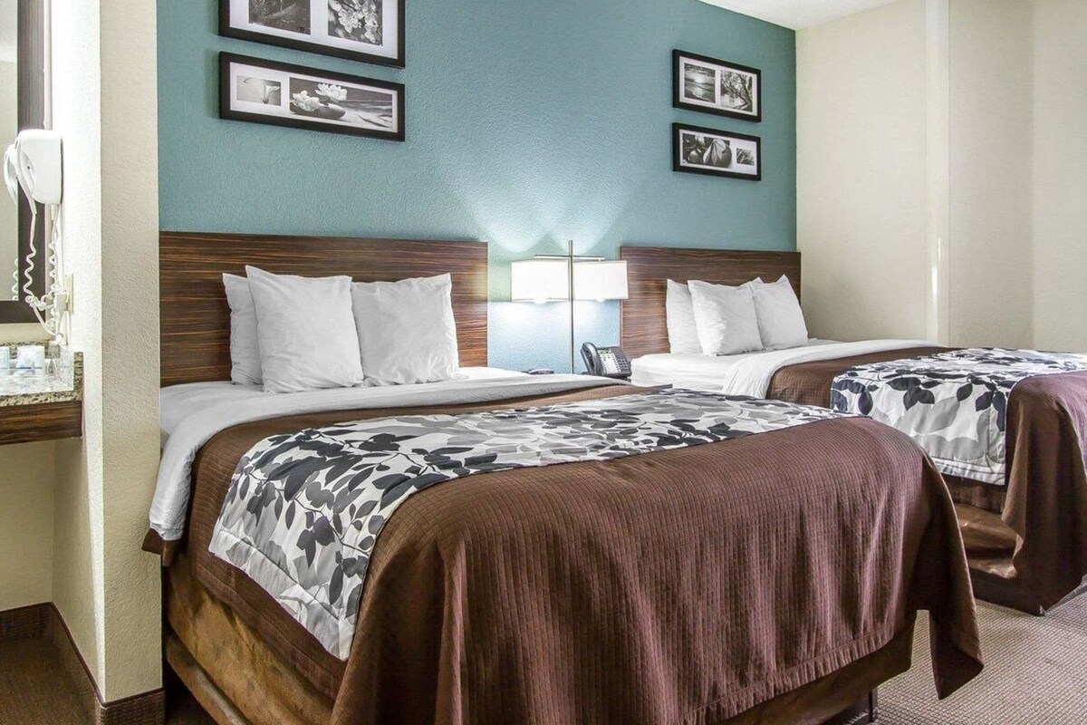 A hotel room with two beds, a nightstand, a lamp, and framed pictures on the wall.
