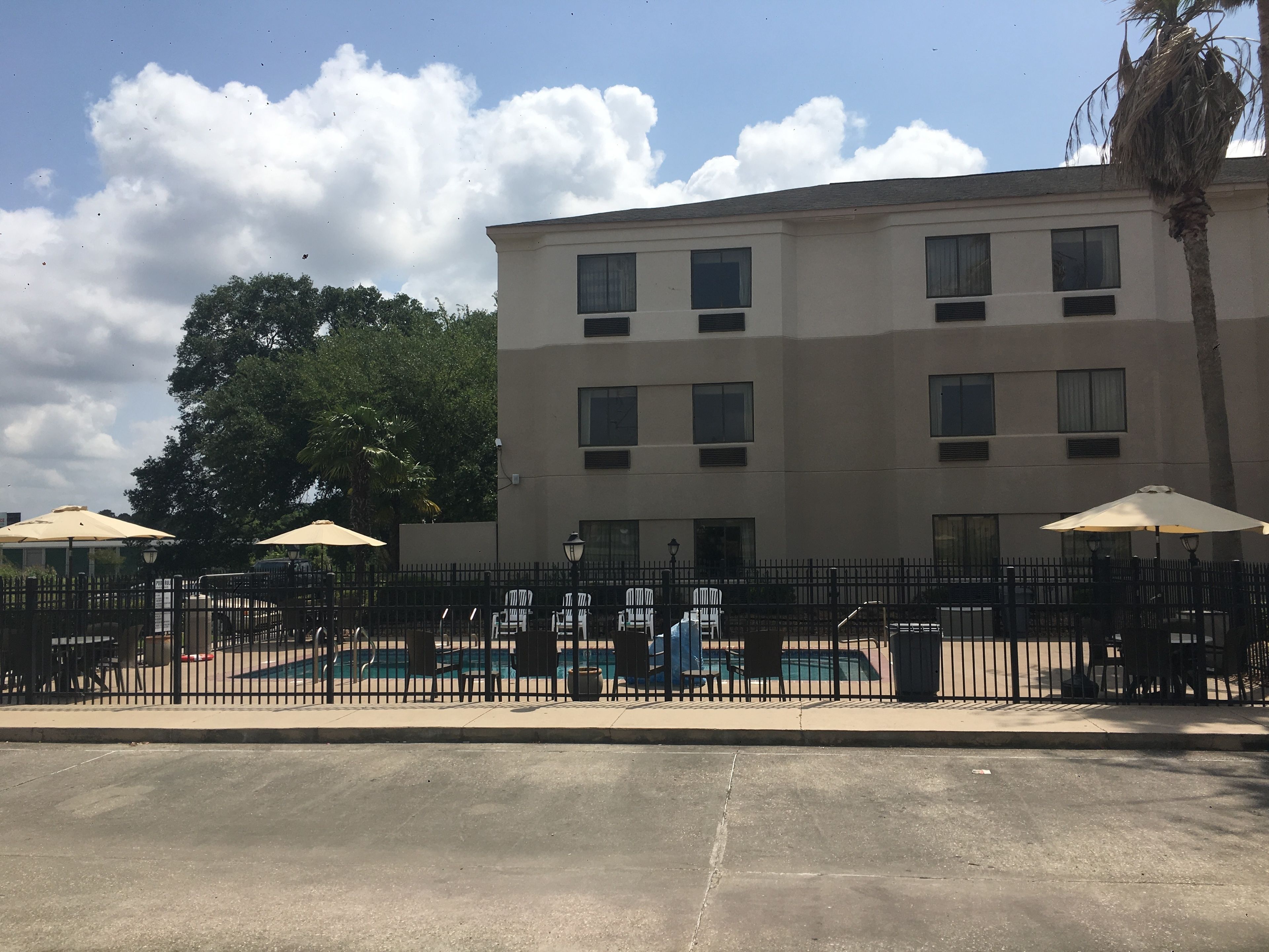 A multi-story building with a pool area, outdoor seating with umbrellas, and a fenced patio.