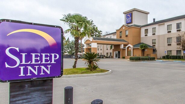 Een Sleep Inn hotel met een opvallend paars bord, een parkeerplaats en een gebouw met veel ramen en een kleine toren.