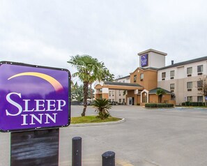 A Sleep Inn hotel with a prominent purple sign, a parking lot, and a building with multiple windows and a small tower. - Sleep Inn Scott/Lafayette West (Scott)