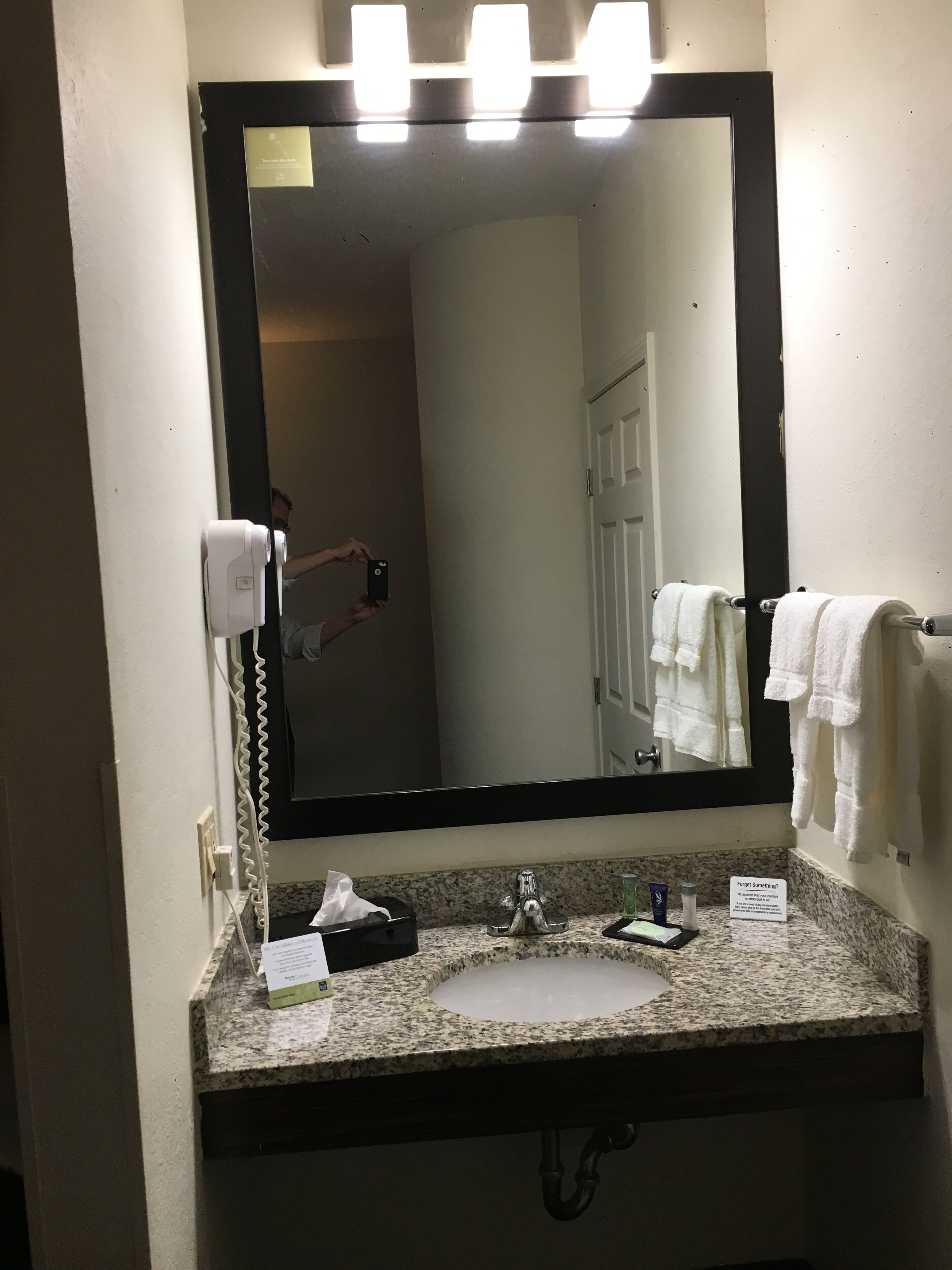 Un baño con un espejo grande, un lavamanos, un perchero para toallas y un secador de pelo.