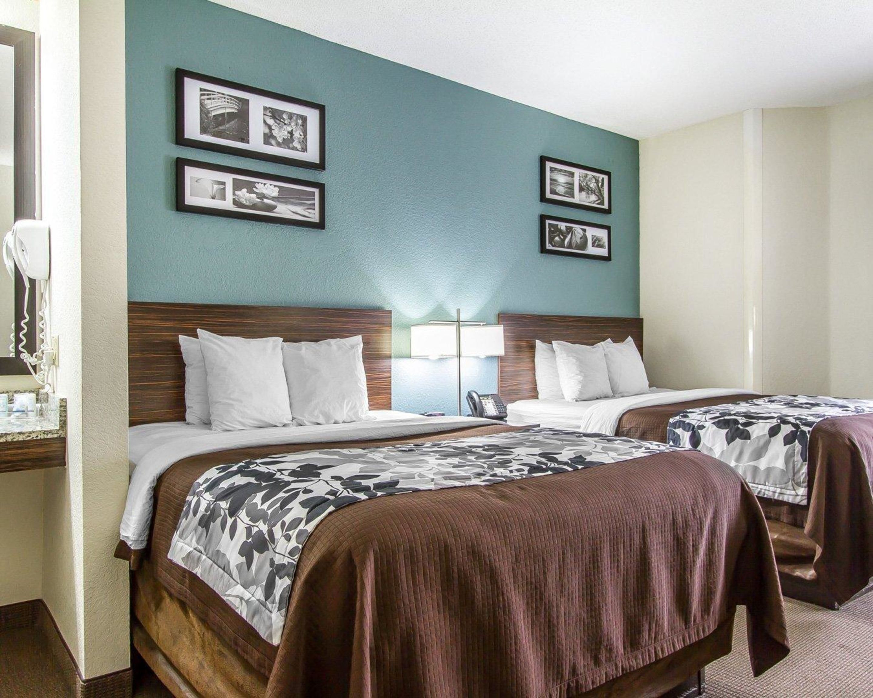 A hotel room with two beds, a nightstand, a lamp, and framed pictures on the wall.