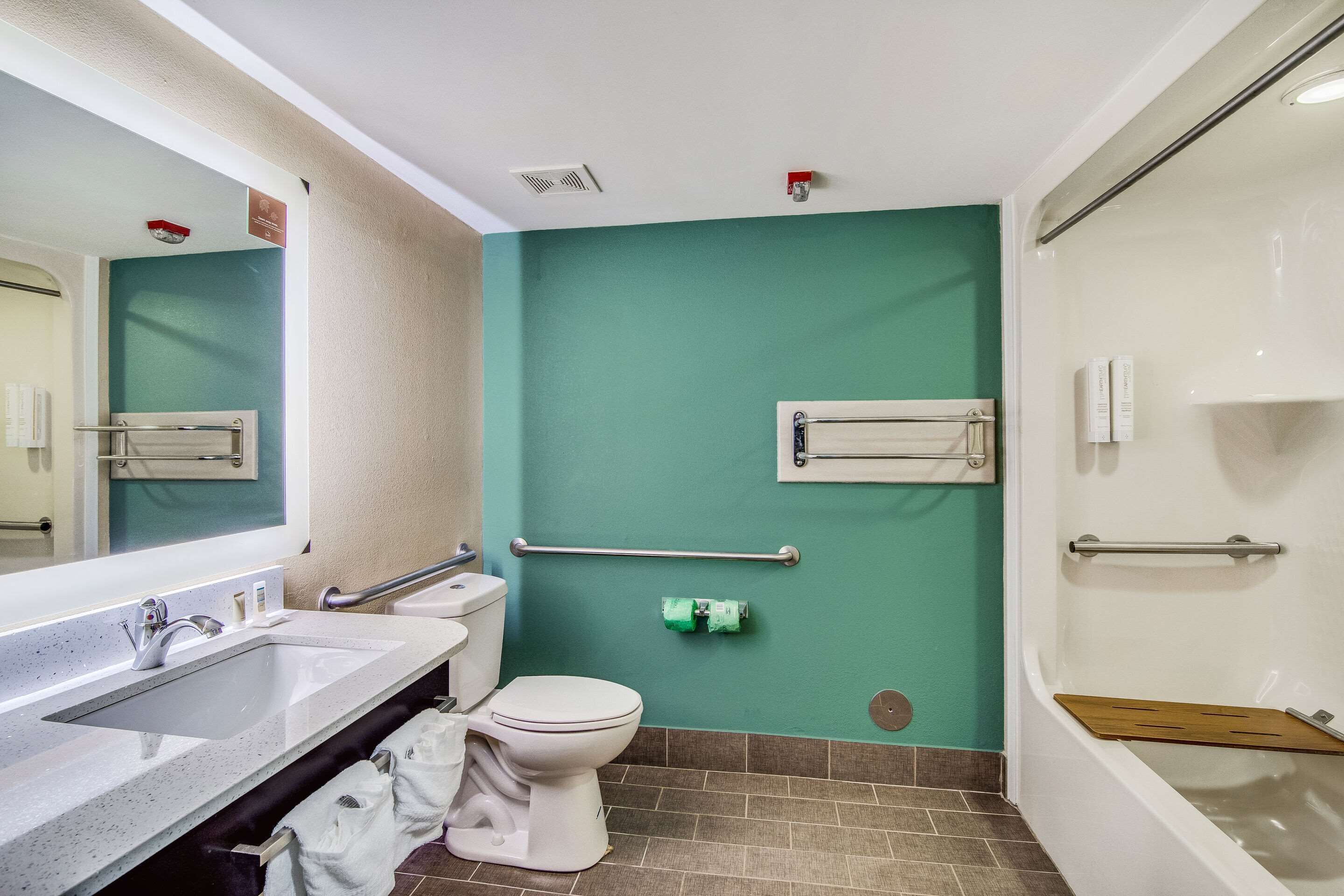 A bathroom with a white sink, toilet, and bathtub. There are handrails and a towel rack.