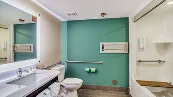 A bathroom with a white sink, toilet, and bathtub. There are handrails and a towel rack.