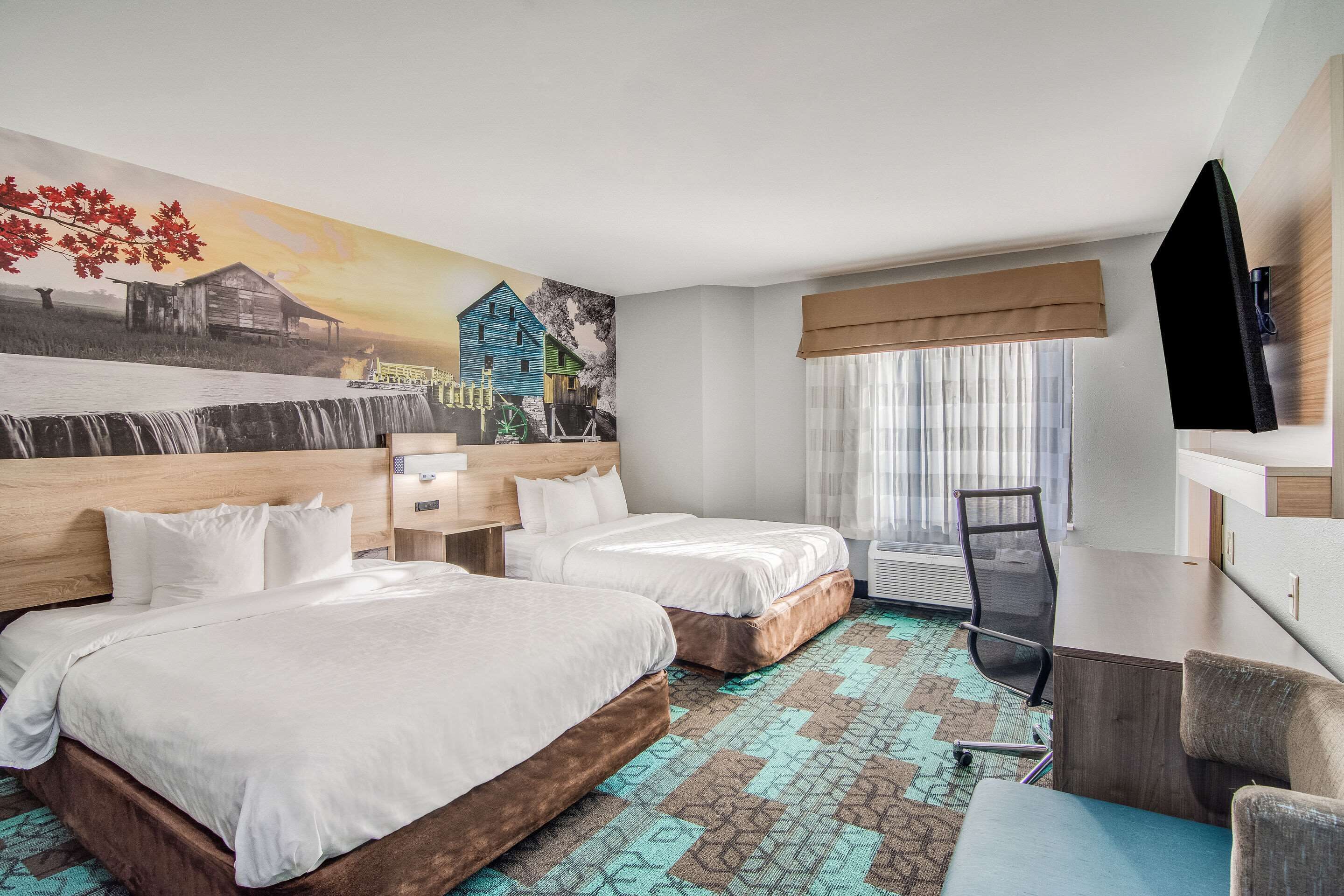 Une chambre d’hôtel avec deux lits, un bureau, une chaise, une télévision et une fresque murale.