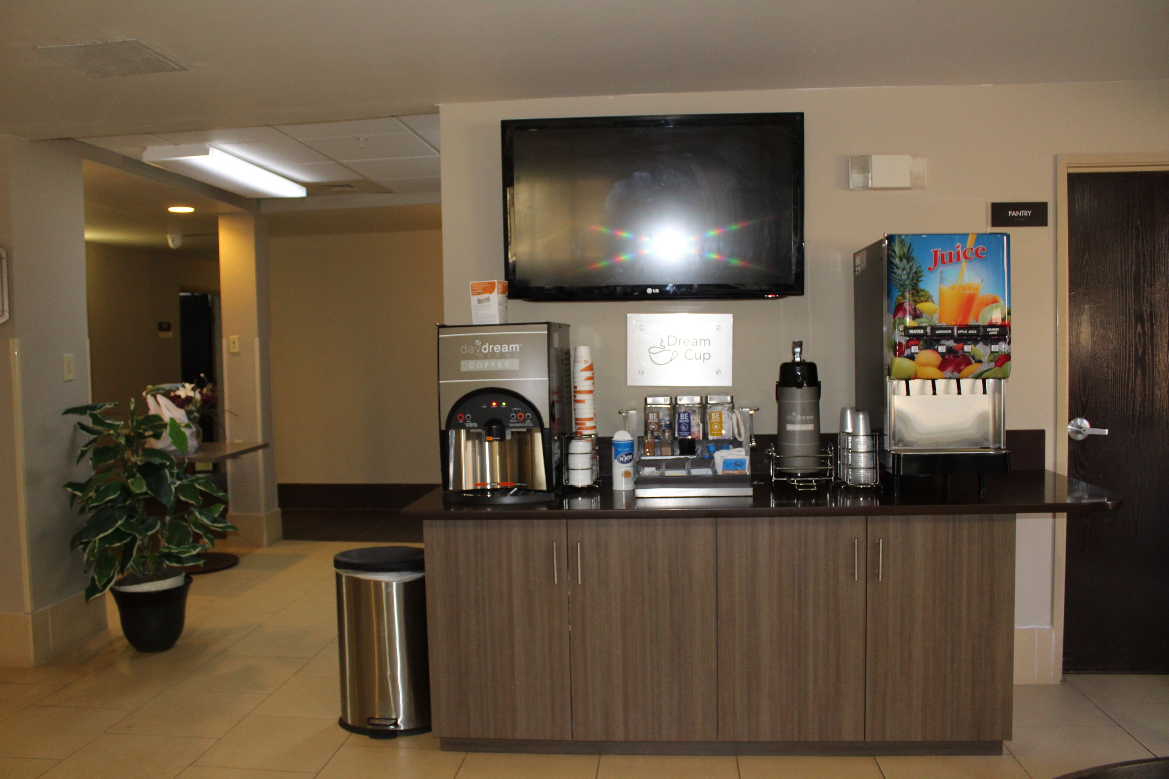 Zona de recepció d'hotel amb una màquina de cafè, un dispensador de suc, una televisió i un cartell per a la despensa.