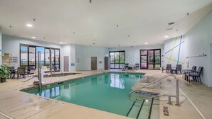 Une piscine intérieure à l’eau claire, entourée de chaises longues et de tables.